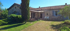 A stone house with a tiled roof, a covered patio, and a garden with a lawn and trees. - Gîte L'Arc-en-Ciel: Spacious Charming House with Central Fireplace (Bournazel)