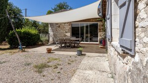 Een stenen gebouw met een terras, een tafel, stoelen, een grote parasol en een grindpad.