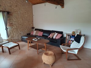 A living room with a sofa, a round coffee table, a wicker ottoman, a wooden chair, and a bookshelf. - Gîte L'Arc-en-Ciel: Spacious Charming House with Central Fireplace (Bournazel)