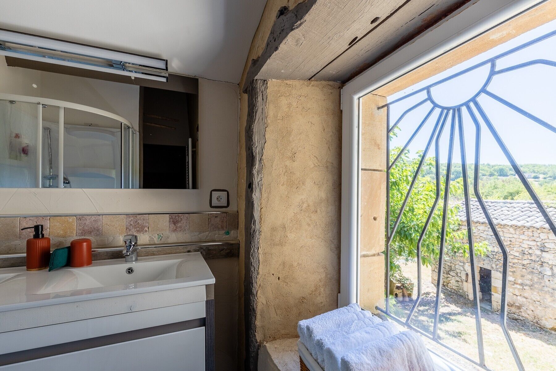A bathroom with a sink, mirror, and window overlooking a garden.