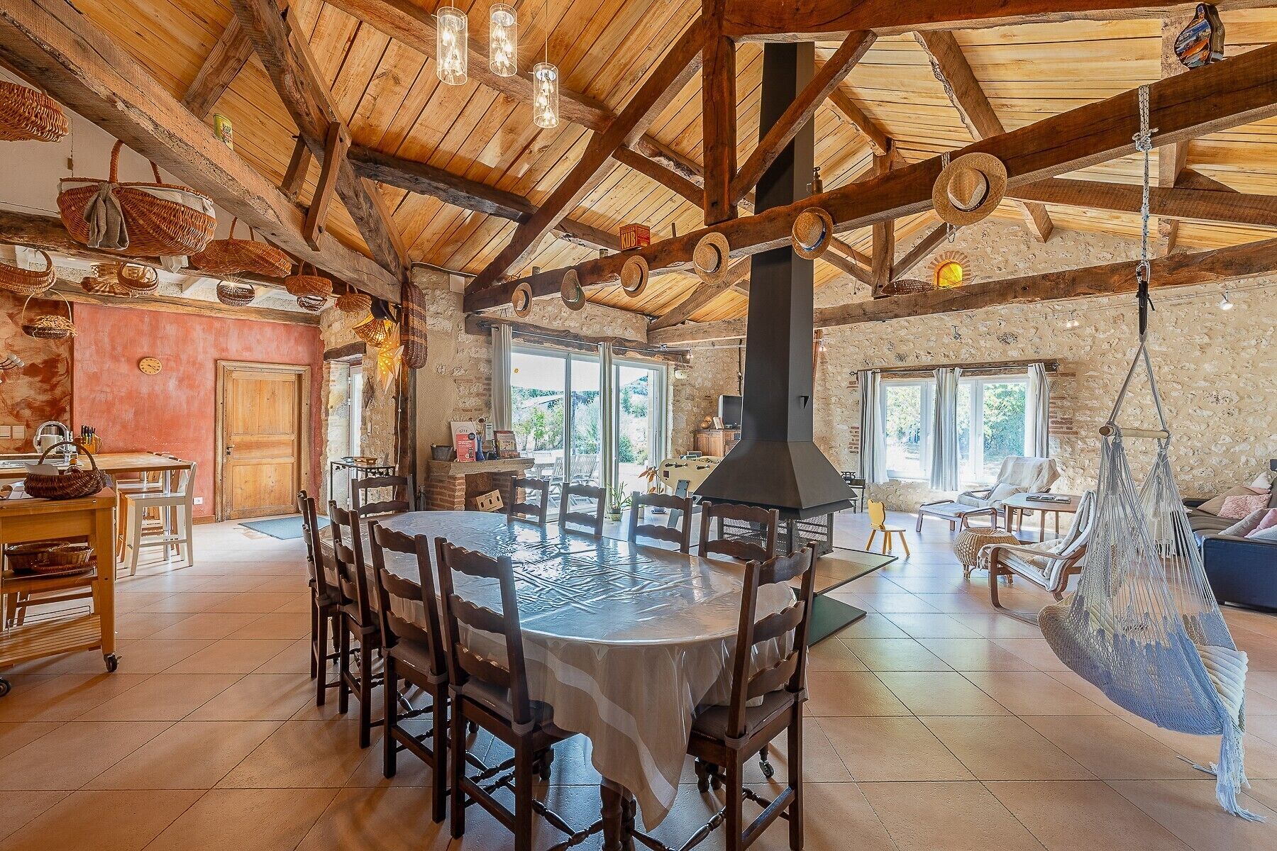 Un intérieur rustique avec une grande table ronde, des poutres en bois et un hamac suspendu.