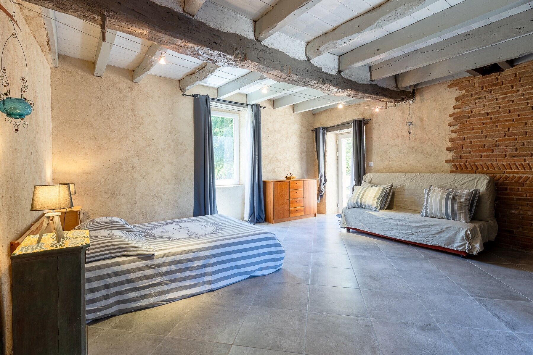 Une pièce comprenant un lit, un canapé, une armoire en bois et une lampe suspendue.