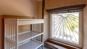 A room with a bunk bed, a window with a metal grill, and a view of the outdoors.