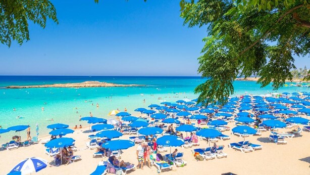 Une plage avec de nombreux parasols bleus et des chaises longues.