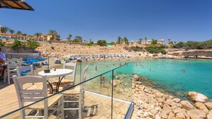 Un complexe hôtelier en bord de mer, doté d’une piscine, de chaises longues et d’une plage rocheuse.