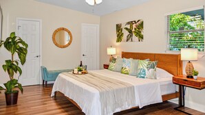 A bedroom with a bed, two bedside tables, a ceiling fan, a window with blinds, and a potted plant. - Vibrant Cuban Style 3BR with AC near Beach & Downtown (Fort Myers)