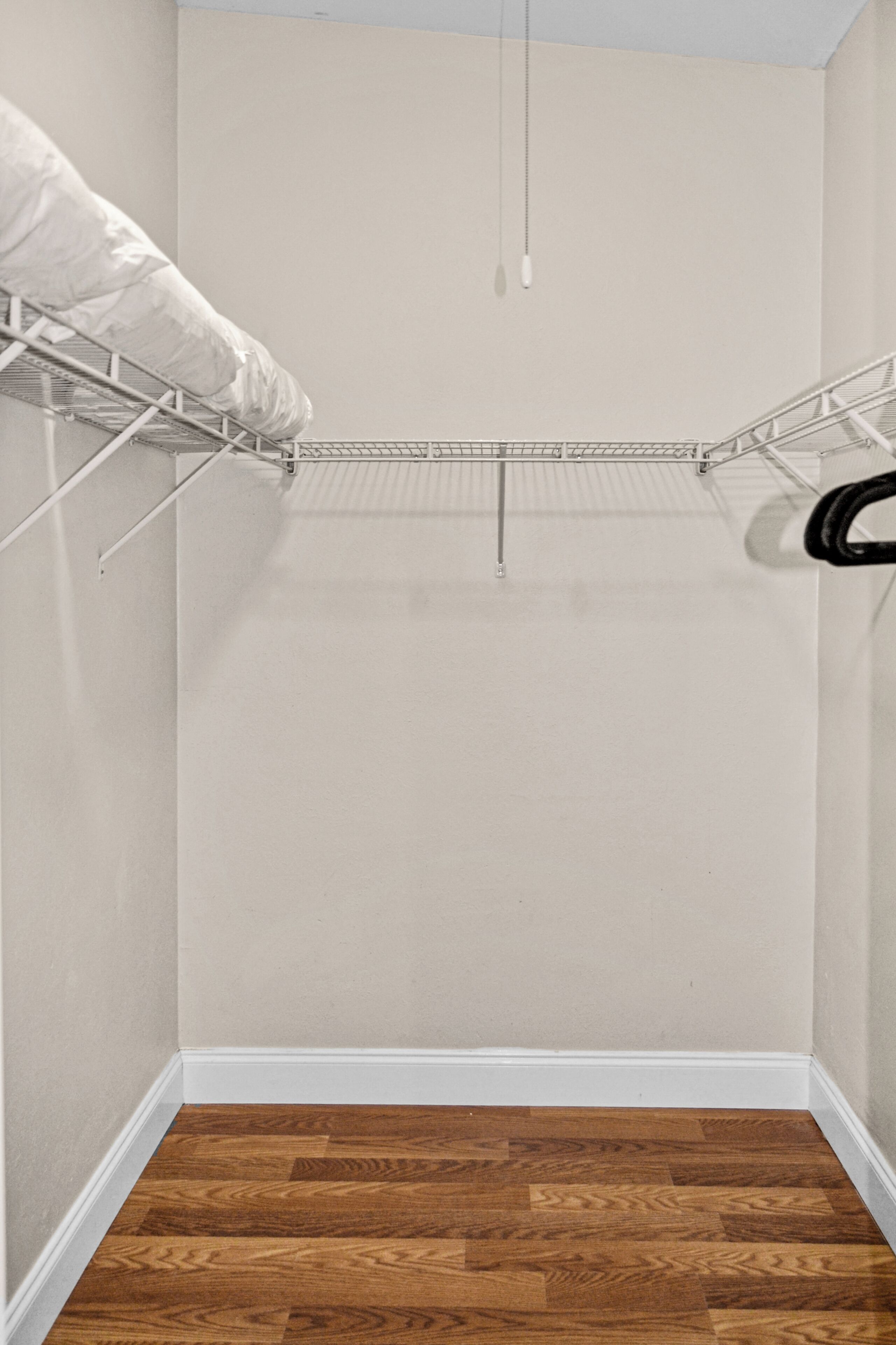 Een hoek van een kamer met een houten vloer, een witte plint en een metalen droogrek aan de muur.