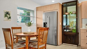 A kitchen with a refrigerator, wooden cabinets, a dining table with chairs, and a window with blinds. - Vibrant Cuban Style 3BR with AC near Beach & Downtown (Fort Myers)