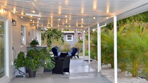 An outdoor patio with a covered seating area, potted plants, and a view of the surrounding greenery. - Vibrant Cuban Style 3BR with AC near Beach & Downtown (Fort Myers)