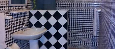 A bathroom with a sink, toilet, and shower area, featuring black and white patterned tiles.