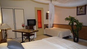 A hotel room with a bed, a desk with a chair, a television, and a plant. - Fana Hotel (Dakar)