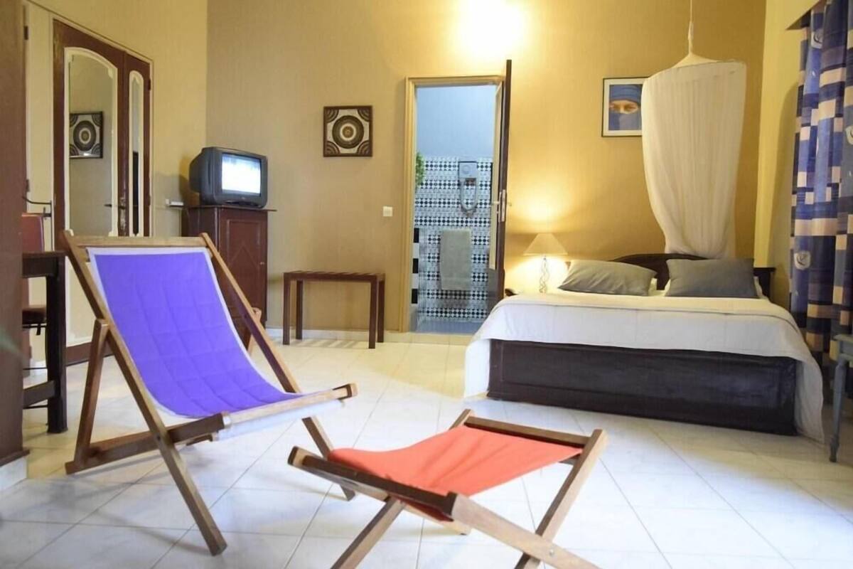 A bedroom with a bed, a television, a chair, and a small table.