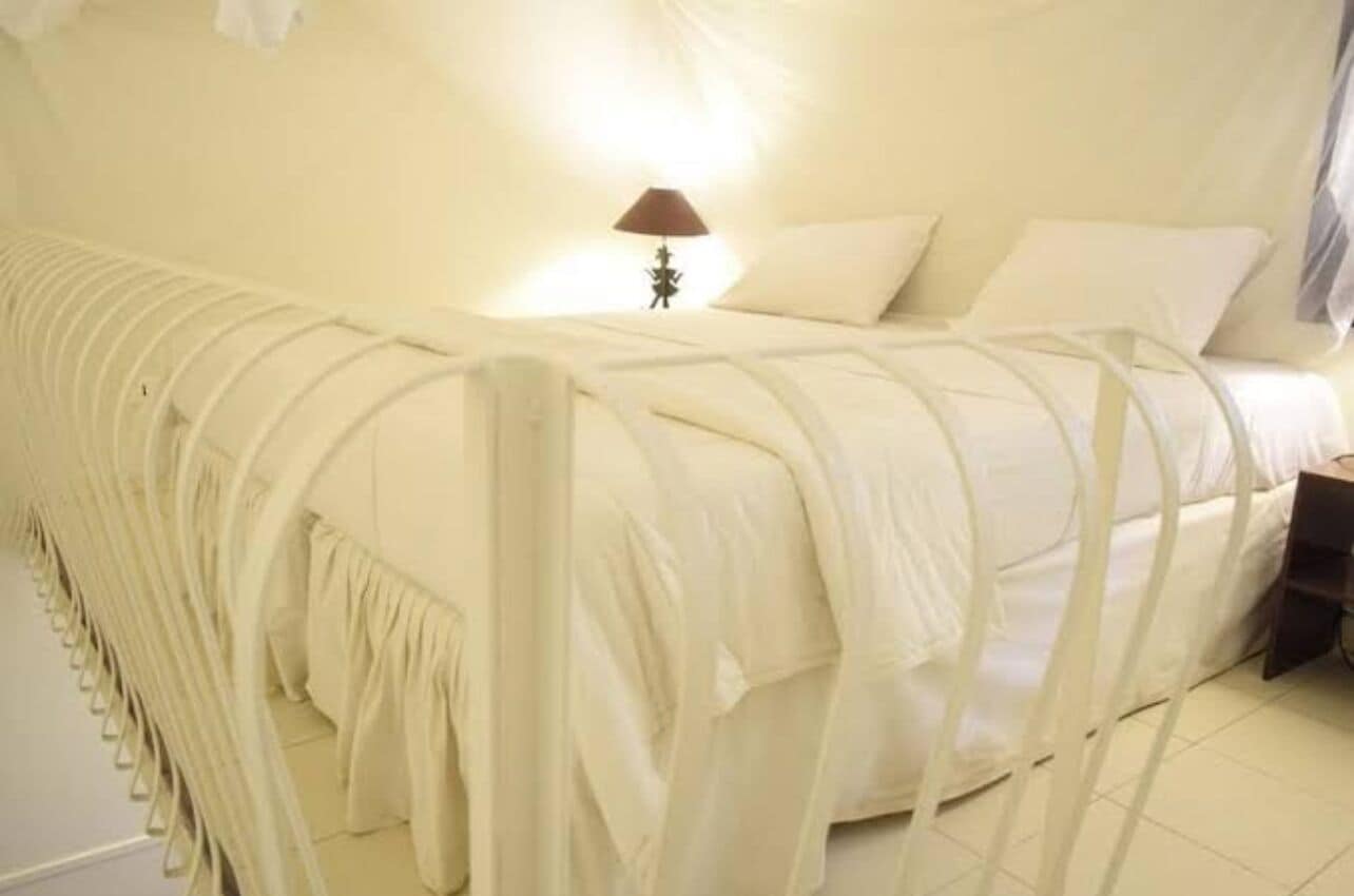 Una cama con cabecera blanca y una lámpara en la mesita de noche.