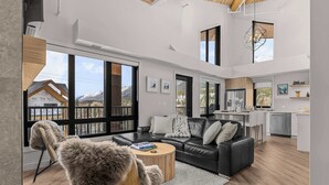 A spacious living area with a sofa, coffee table, and a view of mountains through large windows. - Elevation Hydeaway at Ascent (Canmore)