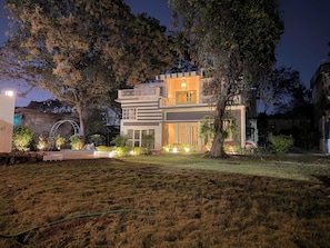 Une maison moderne à deux étages, dotée d’un jardin bien aménagé à l’avant, de grands arbres et d’une arche bien visible.
