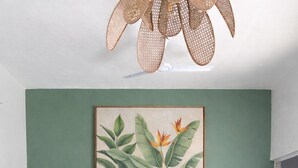 Une pièce avec un mur vert, une console en bois, un tapis tissé et un grand tableau représentant des motifs végétaux.
