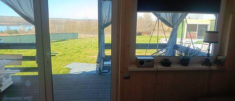Una habitación con puerta de vidrio corrediza que da a un espacio exterior, un ventanal con vistas al exterior y suelo de madera.