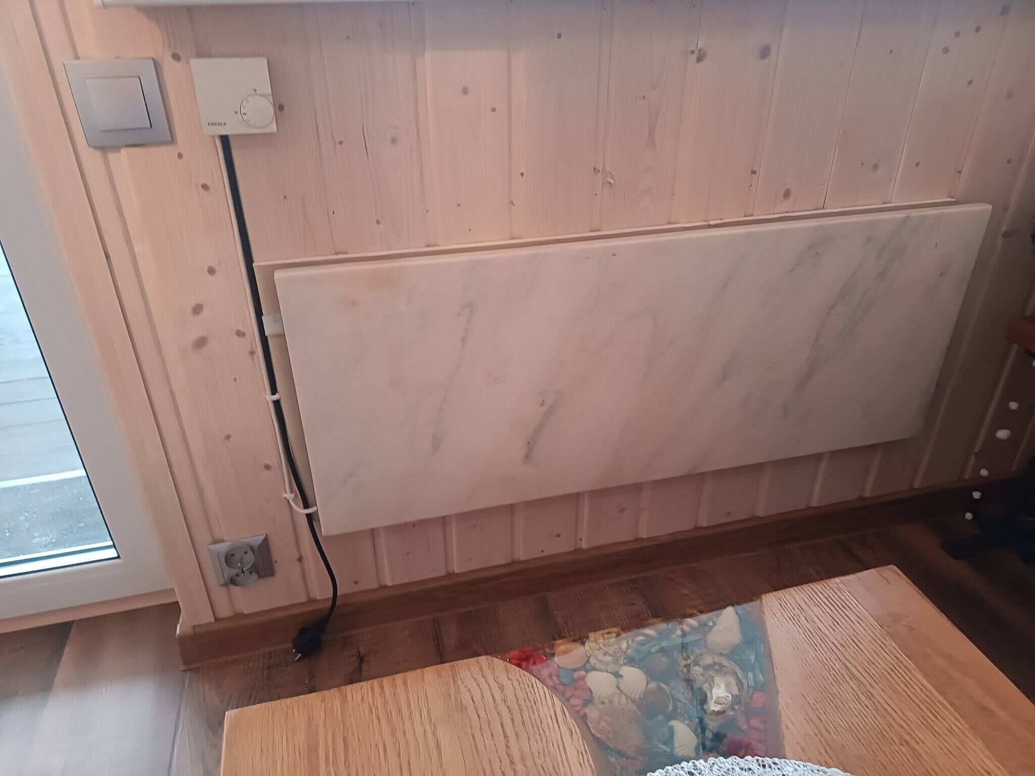 Quarto com parede revestida de madeira, radiador, tomada e janela.