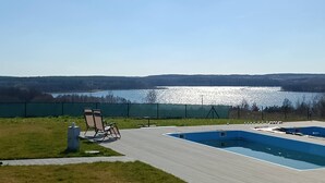 Une piscine avec vue sur un lac, entourée d’une zone délimitée par une clôture et d’une pelouse.