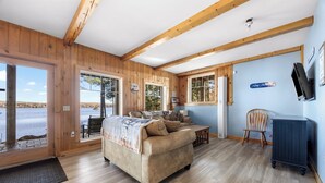 Une pièce aux murs en bois, avec un canapé, un fauteuil, une petite table et une vue sur l’extérieur.