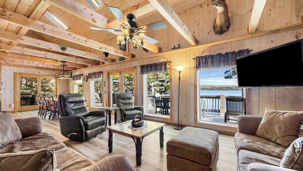 Un intérieur en bois avec un ventilateur de plafond, des fauteuils en cuir, un téléviseur et une tête de cerf accrochée au mur.