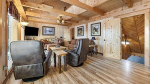 Un intérieur en bois avec un canapé, des fauteuils, un téléviseur et des tableaux encadrés accrochés aux murs.
