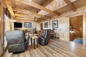 A wooden interior with a sofa, chairs, a television, and framed pictures on the walls.