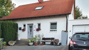 A residential house with a red-tiled roof, a front door, a bench, and a parked car. - 1 room apartment with terrace, quietly situated on the edge of a field. (Remseck am Neckar)