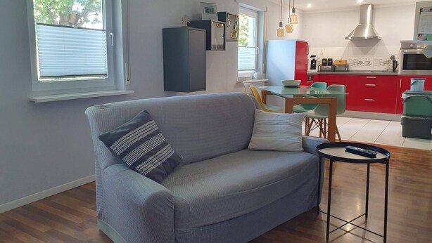 A modern living room with a grey sofa, a small side table, and a dining area with a glass table and chairs. - 1 room apartment with terrace, quietly situated on the edge of a field. (Remseck am Neckar)
