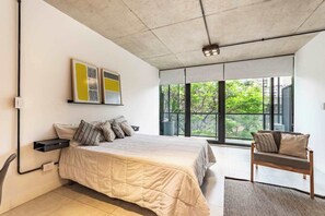 Un dormitorio con cama, una silla, una ventana con vistas y obras de arte en la pared.