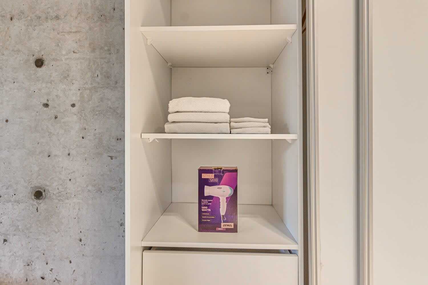 Une étagère blanche sur laquelle sont pliées des serviettes blanches, et une boîte violette posée sur l’étagère du bas.