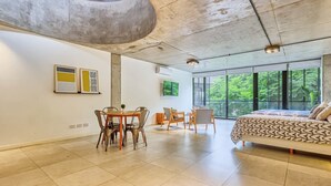 A modern bedroom with a large bed, a dining area with chairs, and a view of greenery through large windows. - NUEVO Loft a 5 minutos de Puerto Madero 2C (Buenos Aires)