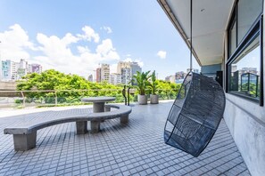 Terraço ao ar livre com um banco curvo, plantas em vasos e vista para a paisagem urbana.