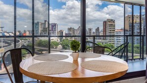 A round wooden table with woven placemats, two chairs, and a potted plant in a room with large windows overlooking a cityscape. - Loft Elegante a 5 Minutos de Puerto Madero 8A (Buenos Aires)