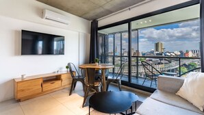 A modern living room with a large window, a flat-screen TV, a wooden console table, a round dining table, and a sofa. - Loft Elegante a 5 Minutos de Puerto Madero 8A (Buenos Aires)