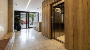 En modern entréhall med en receptionsdisk i trä, en glashiss och en tydlig väg till utgången.