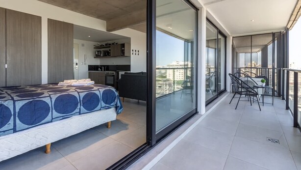 A modern bedroom with a bed, a kitchen, and a balcony with chairs and a table. - NUEVO Loft con Vistas Increíbles a la 9 de Julio (Buenos Aires)