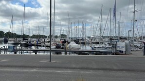 Un port de plaisance où sont amarrés de nombreux voiliers, une promenade pavée et un panier en osier rempli de plantes.