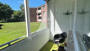 Une pièce avec une grande fenêtre, une chaise noire, une petite table et un mur blanc avec un radiateur.