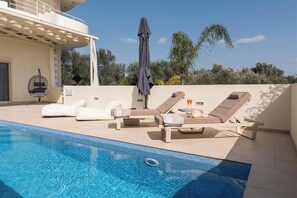 Un espace aménagé au bord de la piscine, avec des chaises longues, un parasol et une chaise.