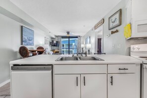 A modern kitchen with a dishwasher, double sink, and white cabinetry. - 🏖️Swim Through Indoor/Outdoor Pool | Private Beach Access | Harbour Place 502 (Orange Beach)
