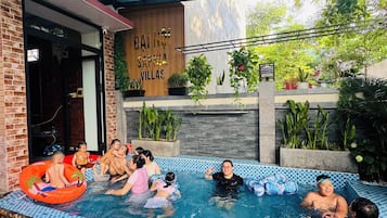 Zona de piscina exterior con techo de cristal, rodeada de plantas y un letrero de madera que dice 'DAI NOI SAPPHIA VILLAS'.