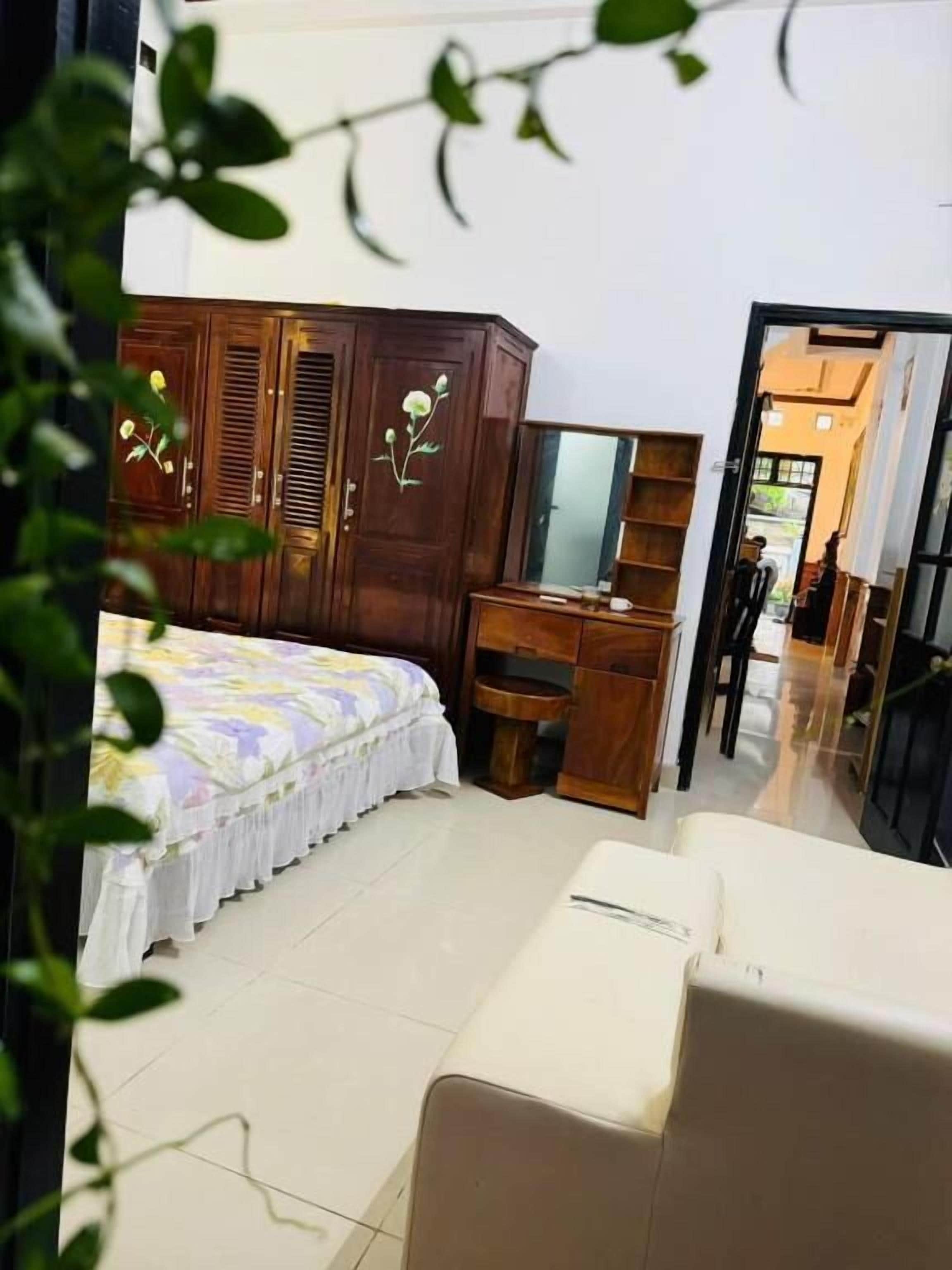 Ein Schlafzimmer mit einem Bett, einem Holzschrank, einem Schreibtisch, einem Spiegel und einem weißen Stuhl.