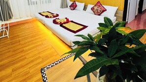 A hotel room with a wooden floor, a bed with red and white bedding, a large potted plant, and a yellow wall. - DAI NOI SAPHIA HOMESTAY (Hue)