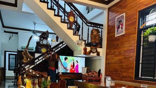 A spacious living area with a staircase, wooden benches, and a television. - DAI NOI SAPHIA HOMESTAY (Hue)