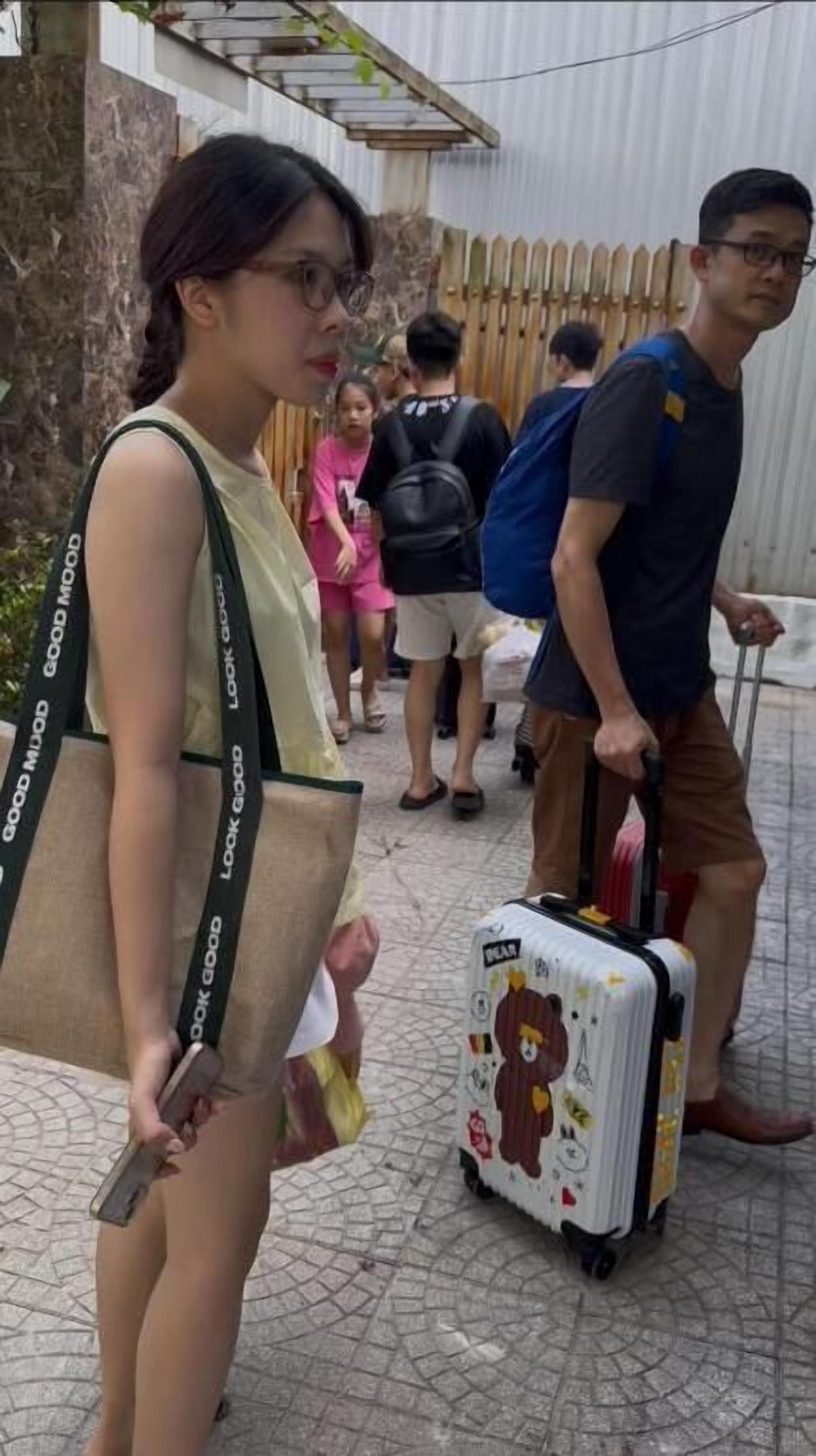 Una persona con una maleta y un bolso caminando por un sendero pavimentado.