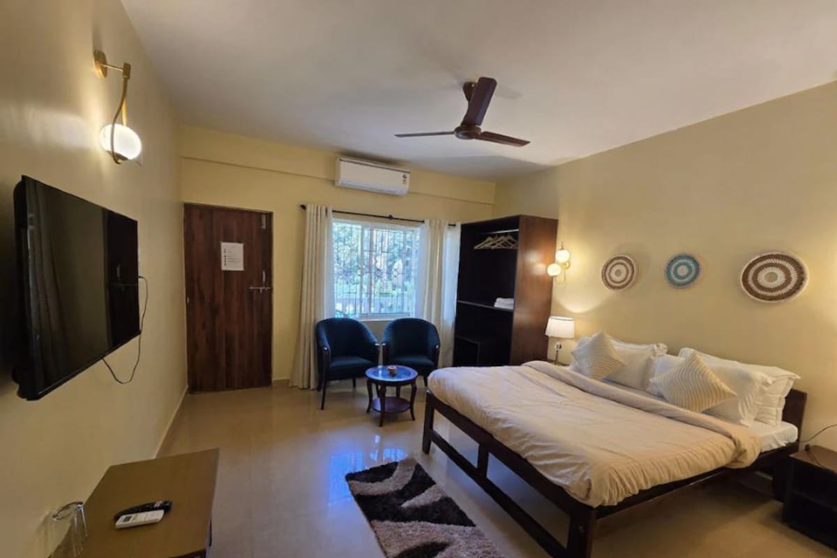 Habitación de hotel con cama, escritorio, silla, televisor y ventilador de techo.
