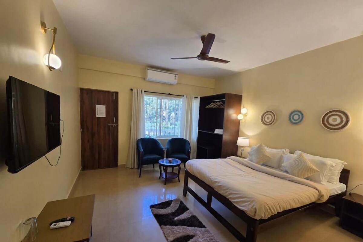 Habitación de hotel con cama, escritorio, silla, televisor y ventilador de techo.