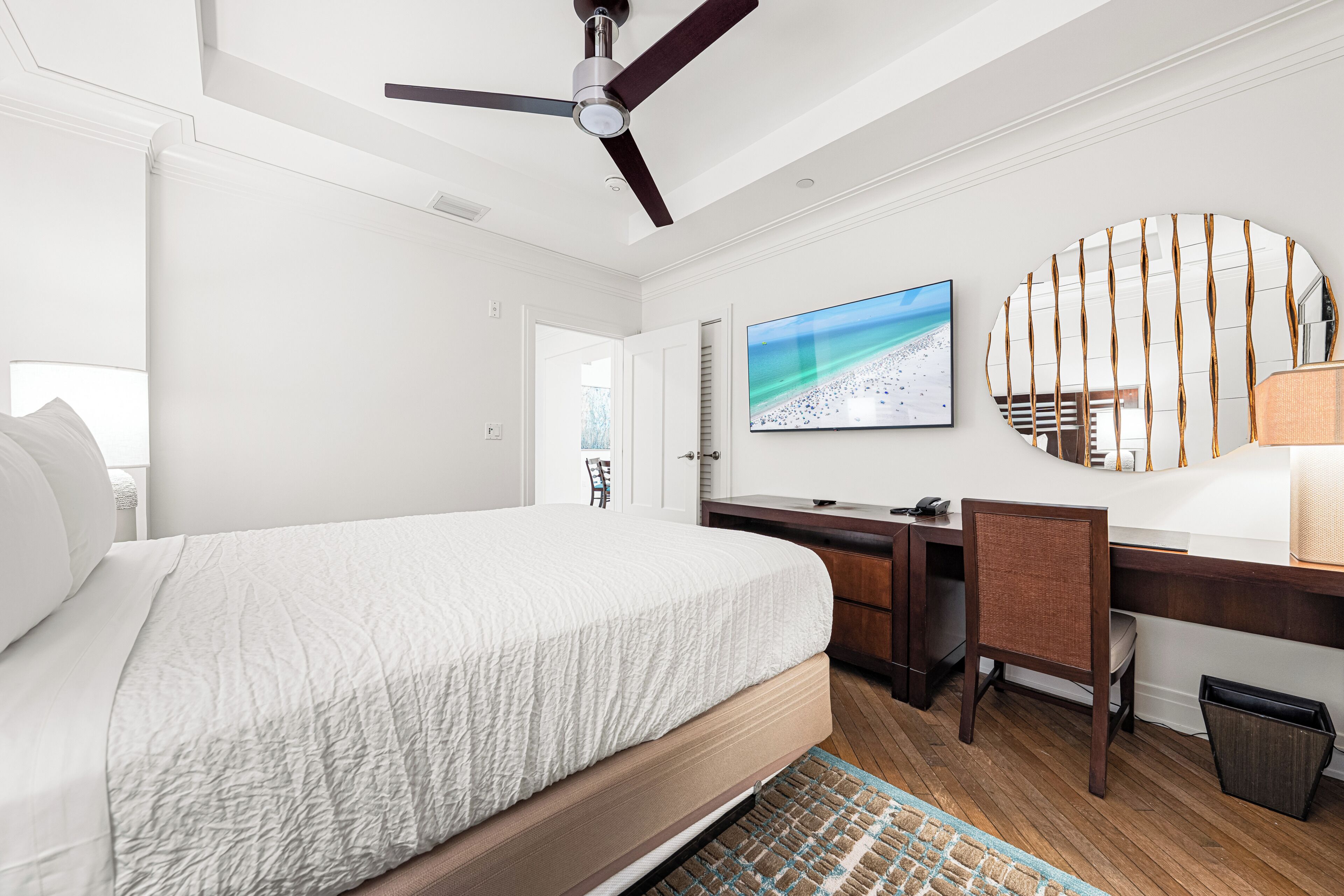 A hotel room with a bed, desk, chair, TV, and a large mirror.