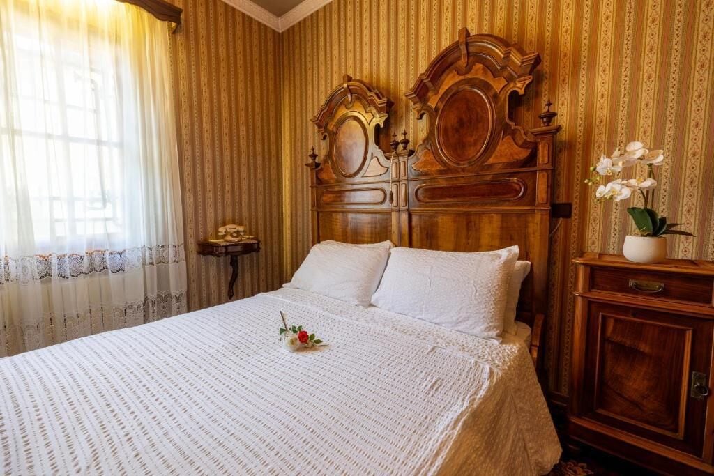 A room with a large bed, a wooden headboard, a nightstand, and a vase with flowers.